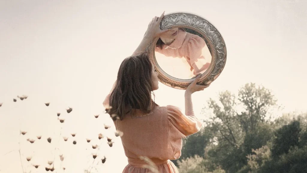 Woman looking into a mirror that she is holding in her hands